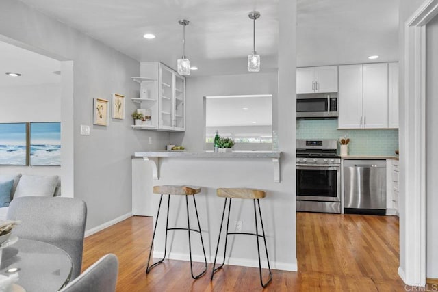 3833 Tomahawk Ln, San Diego, CA 92117 - kitchen featuring stainless steel appliances, a kitchen bar, white cabinets, light wood-style floors, and backsplash