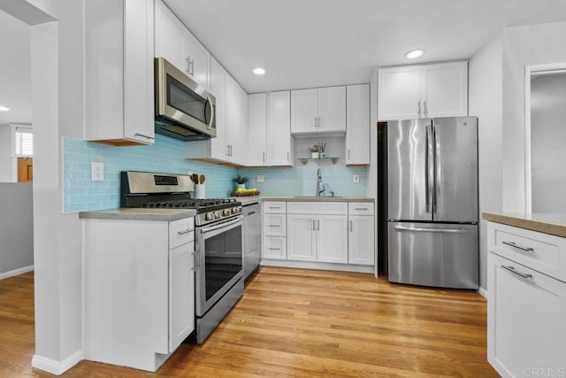3833 Tomahawk Ln, San Diego, CA 92117 - kitchen featuring appliances with stainless steel finishes, light wood-type flooring, light countertops, white cabinetry, and backsplash