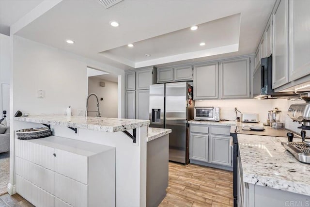 17915 Caminito Pinero Unit 264, San Diego, CA 92128 - kitchen with stainless steel fridge, gray cabinetry, a tray ceiling, light wood-style flooring, and light stone countertops