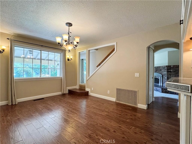 2817 San Verbena Way, Chico, CA 95973 - unfurnished dining area featuring a textured ceiling, a chandelier, arched walkways, dark wood finished floors, and a brick fireplace