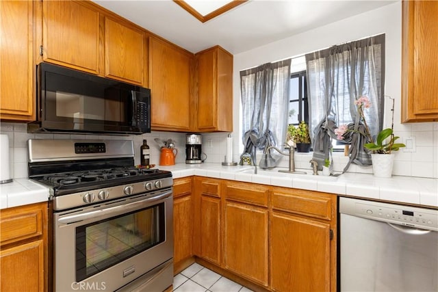 854 N Harbor Blvd, La Habra, CA 90631 - kitchen with appliances with stainless steel finishes, backsplash, brown cabinetry, light tile patterned floors, and tile counters