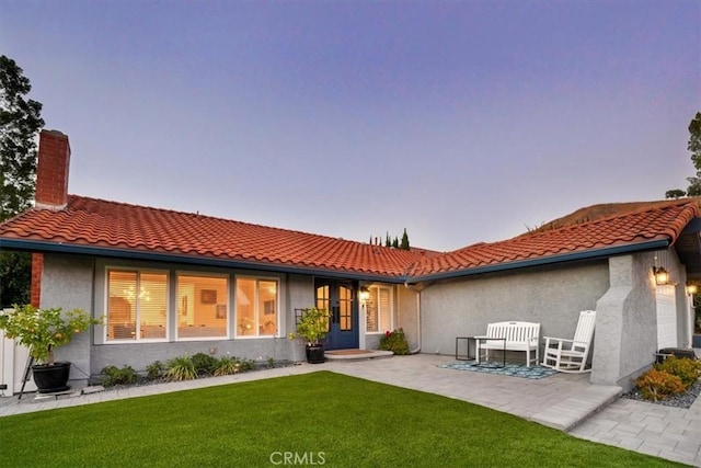 28639 Quaint St, Agoura Hills, CA 91301 - back of property at dusk featuring a lawn, stucco siding, a tiled roof, and a chimney