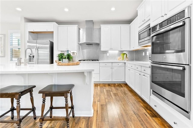 27 Cache St, Rancho Mission Viejo, CA 92694 - kitchen with wall chimney range hood, stainless steel appliances, a kitchen bar, light countertops, and white cabinetry