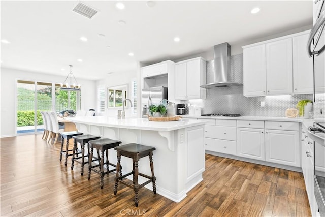 27 Cache St, Rancho Mission Viejo, CA 92694 - kitchen featuring wall chimney exhaust hood, an island with sink, wood finished floors, recessed lighting, and a breakfast bar