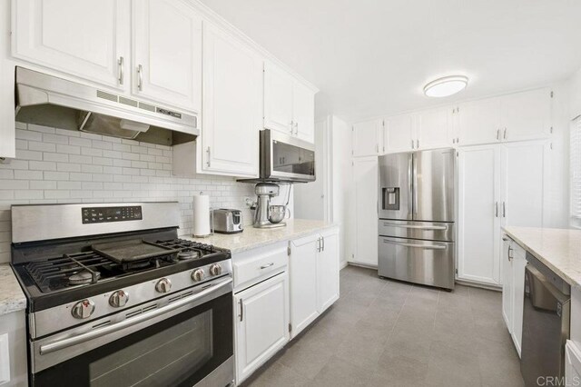 310 Michele Dr, Vista, CA 92084 - kitchen with appliances with stainless steel finishes, under cabinet range hood, white cabinetry, backsplash, and light stone counters