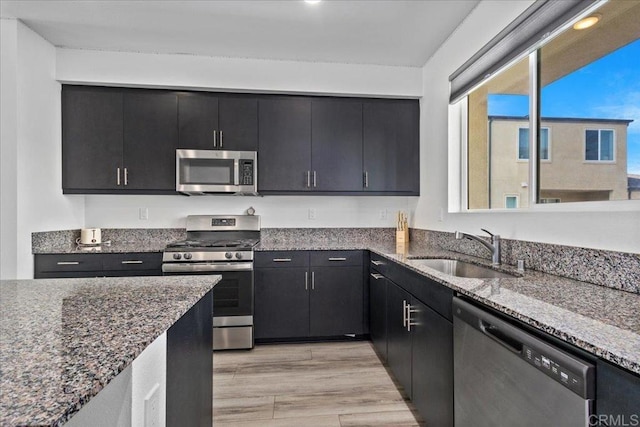 5265 Beachfront Cove St Unit 167, San Diego, CA 92154 - kitchen featuring stainless steel appliances, dark cabinetry, dark stone counters, and light wood-style floors