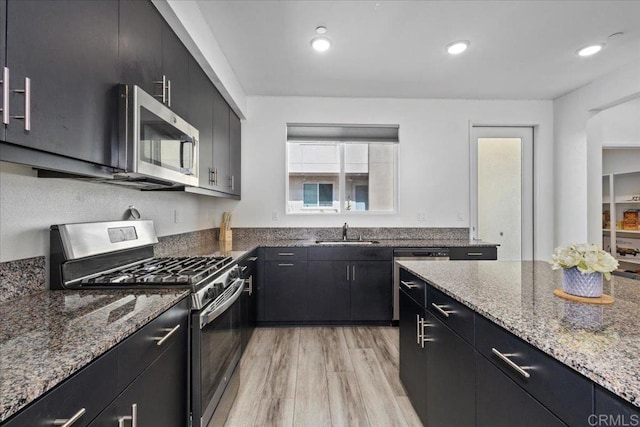 5265 Beachfront Cove St Unit 167, San Diego, CA 92154 - kitchen with stainless steel appliances, dark cabinets, light wood-style flooring, light stone counters, and recessed lighting