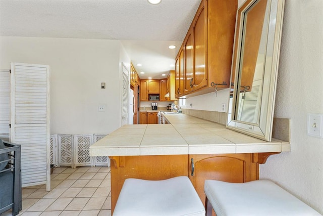 8802 Tyler St, Spring Valley, CA 91977 - kitchen featuring brown cabinets, tile countertops, a peninsula, light tile patterned floors, and a breakfast bar area