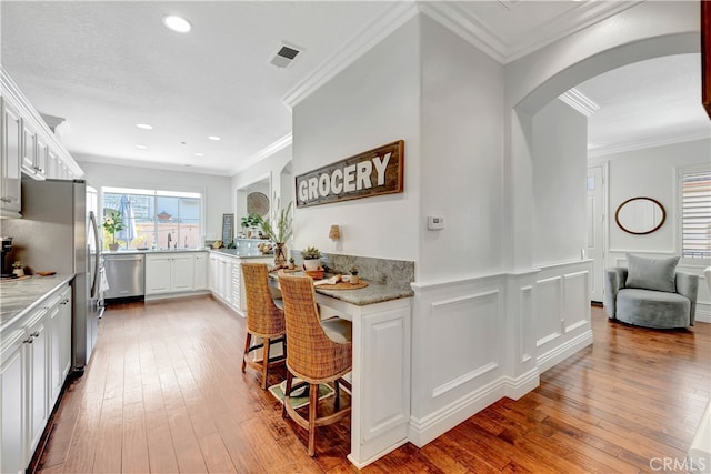 6 Camino Celeste, San Clemente, CA 92673 - kitchen with stainless steel appliances, arched walkways, hardwood / wood-style flooring, crown molding, and white cabinetry