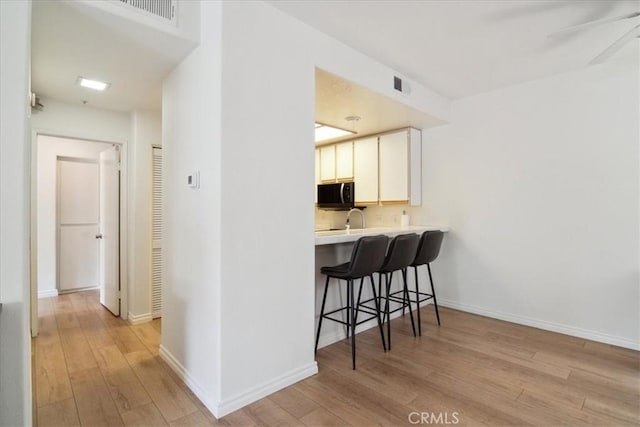 2960 Champion Way Unit 1006, Tustin, CA 92782 - kitchen with black microwave, light wood-style floors, a kitchen breakfast bar, and light countertops