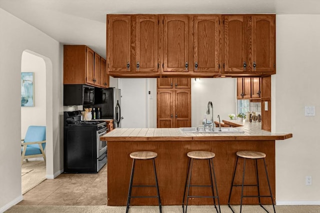 5530 Heidi St, La Mesa, CA 91942 - kitchen with gas stove, black microwave, brown cabinetry, a peninsula, and a breakfast bar area