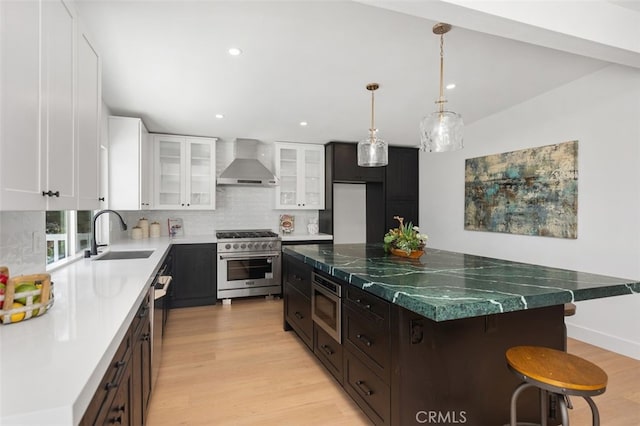 32862 Bluffside Dr, Dana Point, CA 92629 - kitchen with wall chimney exhaust hood, stainless steel appliances, tasteful backsplash, light wood-style flooring, and a kitchen bar