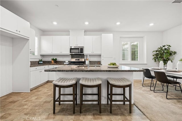 5603 Kate Way Unit 4, Fontana, CA 92336 - kitchen with appliances with stainless steel finishes, a breakfast bar, an island with sink, white cabinetry, and dark stone countertops
