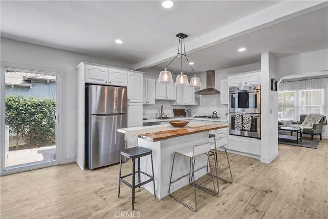 2255 Cota Ave, Long Beach, CA 90810 - kitchen featuring appliances with stainless steel finishes, wall chimney range hood, butcher block countertops, white cabinetry, and healthy amount of natural light