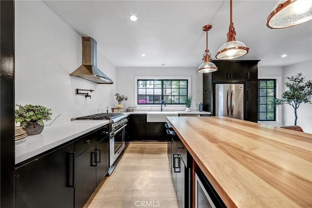 3735 Division St, Los Angeles, CA 90065 - kitchen featuring wall chimney range hood, appliances with stainless steel finishes, dark cabinets, butcher block countertops, and recessed lighting