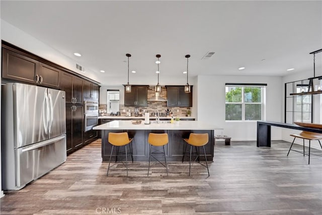 23 Vasto St, Rancho Mission Viejo, CA 92694 - kitchen featuring appliances with stainless steel finishes, light wood-type flooring, wall chimney exhaust hood, dark brown cabinets, and light countertops