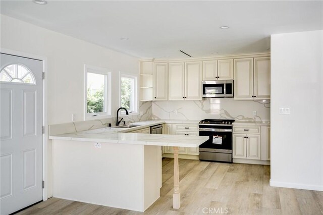 1038 N Columbus Ave, Glendale, CA 91202 - kitchen featuring appliances with stainless steel finishes, light wood finished floors, a peninsula, backsplash, and cream cabinets