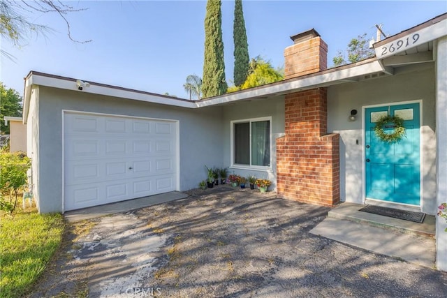 26919 Villa Ave, Highland, CA 92346 - property entrance with a chimney, stucco siding, driveway, and a garage
