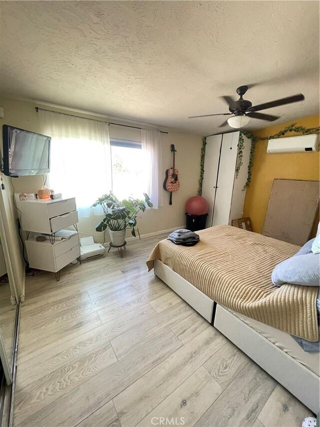10623 4th Ave, Hesperia, CA 92345 - bedroom featuring a wall mounted AC, light wood-style floors, a textured ceiling, and ceiling fan