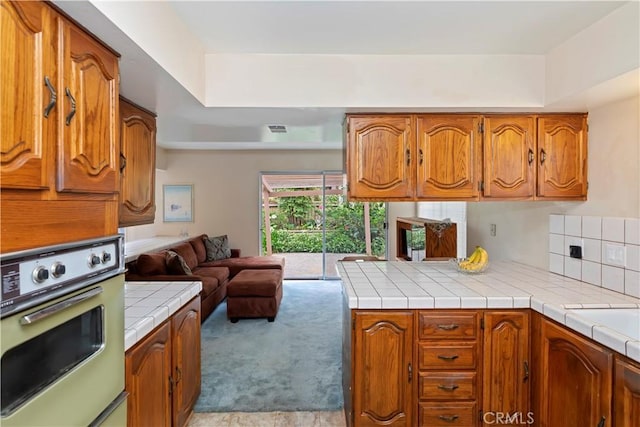 10 Mann St, Irvine, CA 92612 - kitchen featuring white oven, open floor plan, brown cabinetry, tile counters, and light carpet