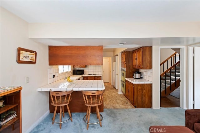 10 Mann St, Irvine, CA 92612 - kitchen featuring tile counters, oven, brown cabinetry, light colored carpet, and decorative backsplash