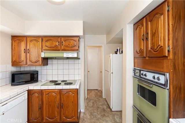 10 Mann St, Irvine, CA 92612 - kitchen with white appliances, under cabinet range hood, brown cabinets, tasteful backsplash, and tile counters