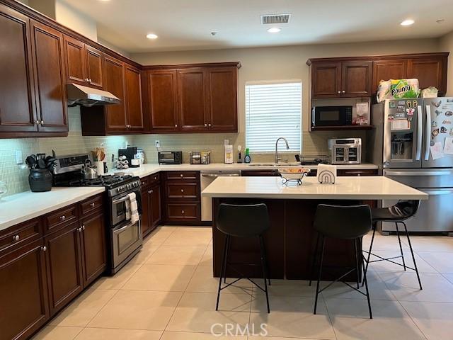 513 E Water St, Anaheim, CA 92805 - kitchen featuring stainless steel appliances, under cabinet range hood, a kitchen breakfast bar, tasteful backsplash, and recessed lighting