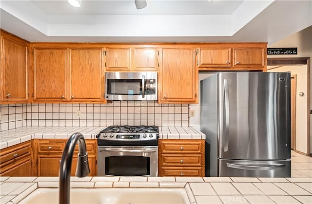 24050 Basin Harbor Ct, Tehachapi, CA 93561 - kitchen featuring appliances with stainless steel finishes, a tray ceiling, tile countertops, and decorative backsplash