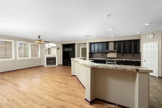 12975 Cambridge Ct, Chino, CA 91710 - kitchen featuring wall chimney range hood, tasteful backsplash, a chandelier, a fireplace with raised hearth, and light stone counters