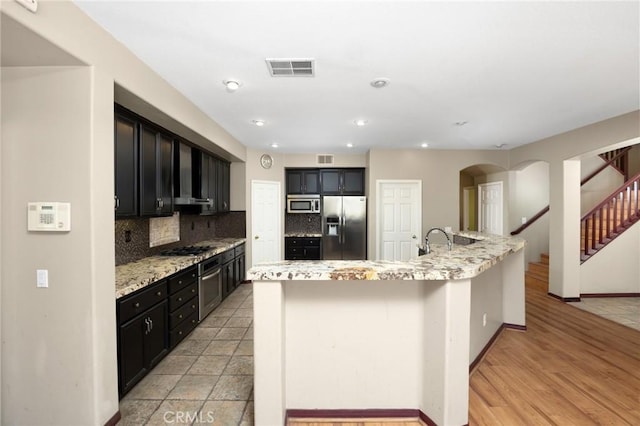 12975 Cambridge Ct, Chino, CA 91710 - kitchen featuring appliances with stainless steel finishes, dark cabinetry, backsplash, arched walkways, and light stone counters