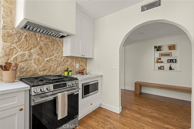 4131 Edgehill Dr, Los Angeles, CA 90008 - kitchen with appliances with stainless steel finishes, custom exhaust hood, arched walkways, light wood finished floors, and decorative backsplash