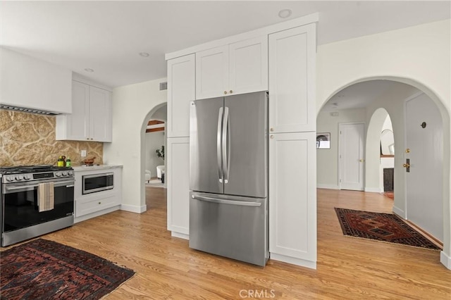 4131 Edgehill Dr, Los Angeles, CA 90008 - kitchen with appliances with stainless steel finishes, tasteful backsplash, white cabinets, light wood-style floors, and arched walkways