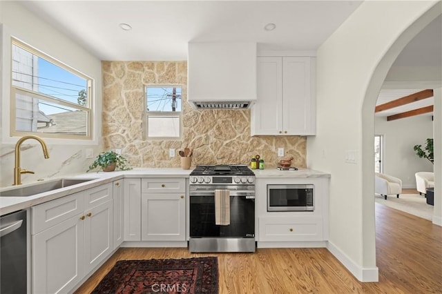 4131 Edgehill Dr, Los Angeles, CA 90008 - kitchen featuring stainless steel appliances, custom exhaust hood, arched walkways, backsplash, and light wood finished floors