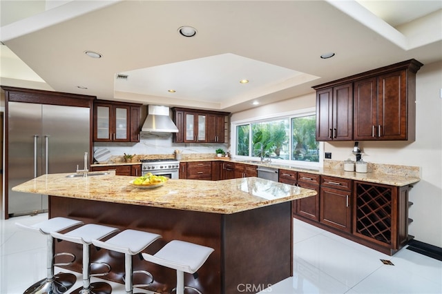 275 E 24th St, Upland, CA 91784 - kitchen featuring wall chimney exhaust hood, premium appliances, a raised ceiling, an island with sink, and light stone counters