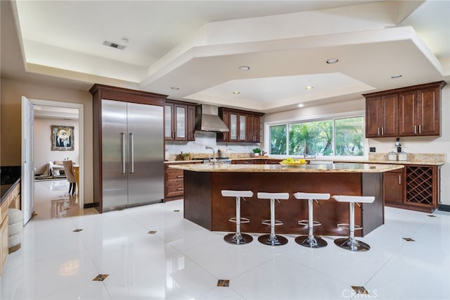 275 E 24th St, Upland, CA 91784 - kitchen featuring a tray ceiling, stainless steel built in refrigerator, wall chimney range hood, a kitchen island, and a breakfast bar area