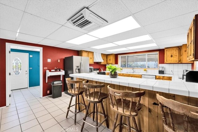 1638 Hales Dr Unit 29, Palms, CA 92277 - kitchen featuring tile counters, a paneled ceiling, range with electric stovetop, a peninsula, and brown cabinets