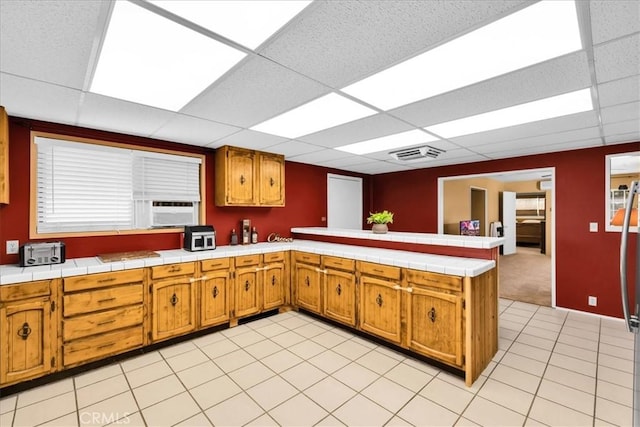 1638 Hales Dr Unit 29, Palms, CA 92277 - kitchen with a peninsula, a paneled ceiling, brown cabinets, light tile patterned flooring, and cooling unit