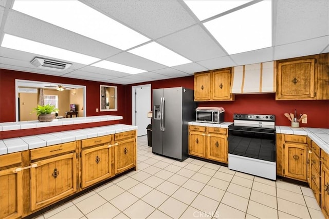 1638 Hales Dr Unit 29, Palms, CA 92277 - kitchen featuring electric stove, stainless steel fridge, wall chimney exhaust hood, brown cabinets, and a paneled ceiling