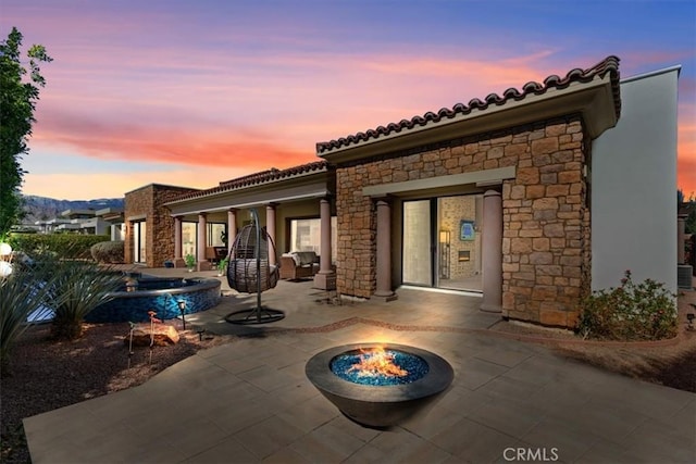 17 Emerald Ct, Rancho Mirage, CA 92270 - back of house at dusk featuring a patio, a fire pit, stone siding, and a tiled roof