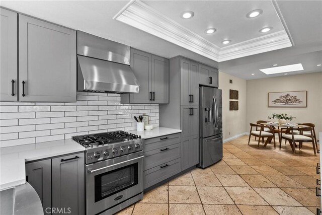 3891 Hunters Grove Ct, Moorpark, CA 93021 - kitchen featuring appliances with stainless steel finishes, wall chimney exhaust hood, ornamental molding, a tray ceiling, and gray cabinets