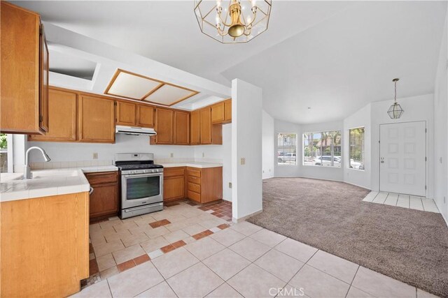 4706 Crestmont Pl, Oceanside, CA 92056 - kitchen with stainless steel range with gas cooktop, under cabinet range hood, light colored carpet, light tile patterned flooring, and brown cabinetry