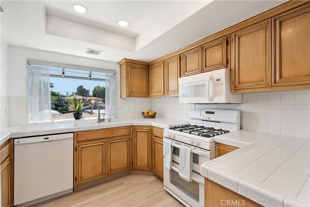 14853 Hartsook St Unit 106, Sherman Oaks, CA 91403 - kitchen with white appliances, brown cabinetry, light wood-type flooring, tile counters, and backsplash