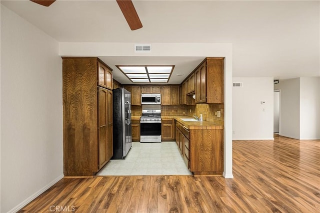 14000 Cerise Ave, Hawthorne, CA 90250 - kitchen featuring stainless steel appliances, a ceiling fan, light wood finished floors, backsplash, and brown cabinetry