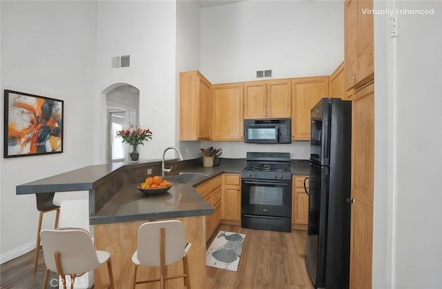 19431 Rue De Valore Unit 5C, Lake Forest, CA 92610 - kitchen featuring black appliances, a towering ceiling, dark countertops, a peninsula, and light wood finished floors