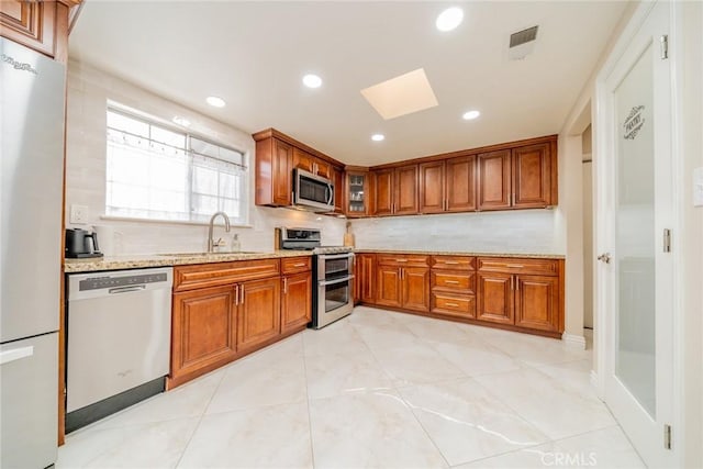 18210 Deauville Dr, Victorville, CA 92395 - kitchen featuring stainless steel appliances, brown cabinets, a skylight, light stone countertops, and tasteful backsplash