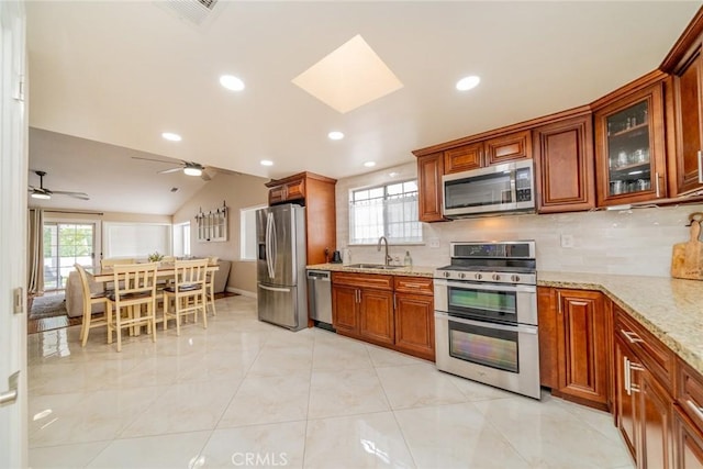 18210 Deauville Dr, Victorville, CA 92395 - kitchen featuring stainless steel appliances, lofted ceiling, a skylight, light stone counters, and brown cabinetry