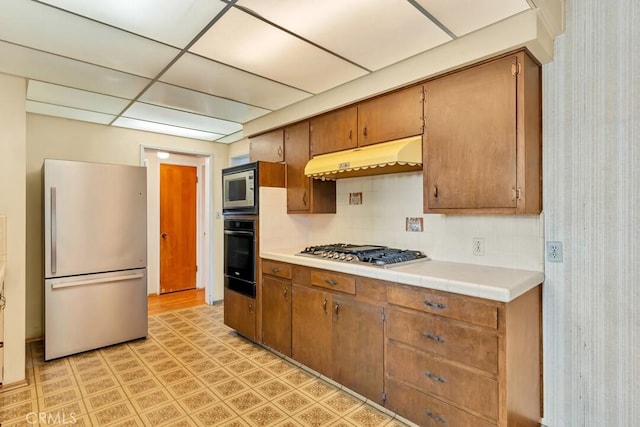 4760 73rd St, La Mesa, CA 91942 - kitchen featuring appliances with stainless steel finishes, under cabinet range hood, backsplash, brown cabinetry, and a drop ceiling