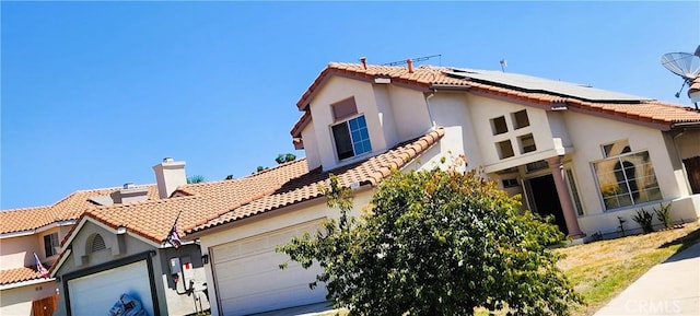 186 S Massachusetts St, Lake Elsinore, CA 92530 - view of front facade with a tile roof, roof mounted solar panels, stucco siding, a garage, and a chimney