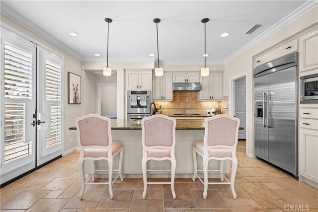 35 Twin Gables, Irvine, CA 92620 - kitchen with built in appliances, under cabinet range hood, stone tile floors, backsplash, and a kitchen breakfast bar