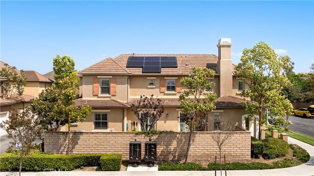 35 Twin Gables, Irvine, CA 92620 - view of front facade with stucco siding, roof mounted solar panels, a chimney, and a tiled roof